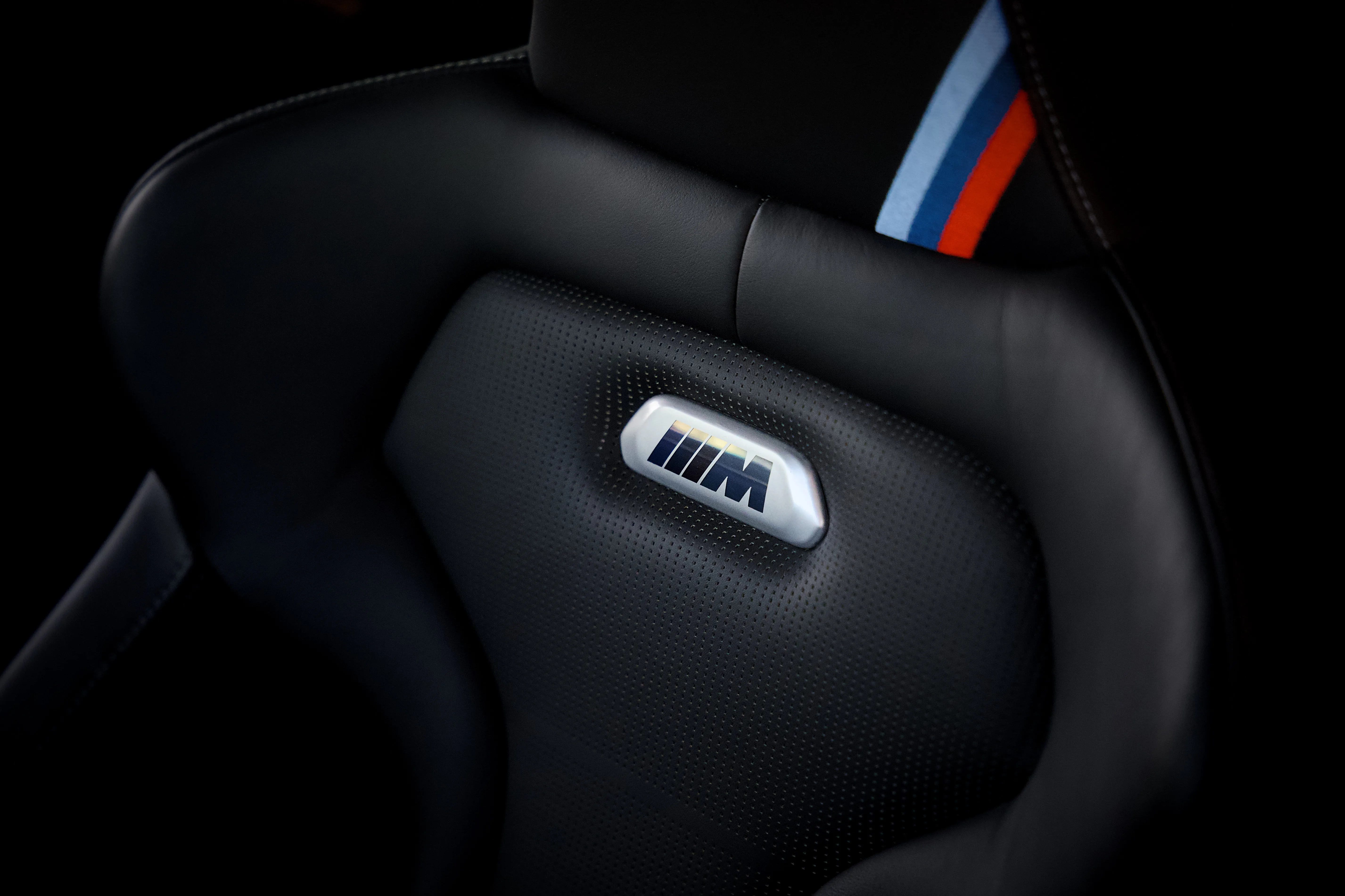 Close-up of a perforated black leather BMW M sport seat with the M badge emblem and tricolor M stripe detail