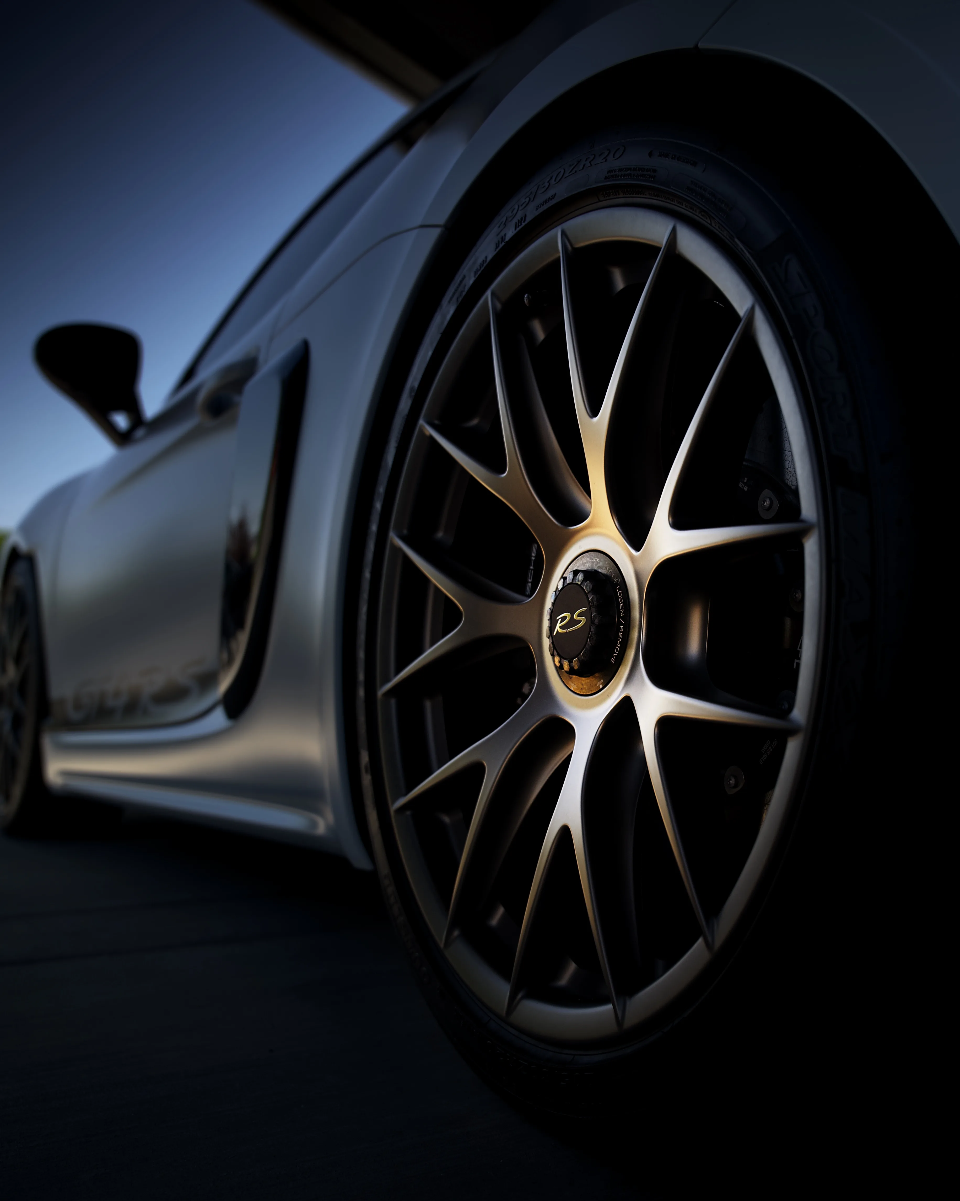 Low-angle close-up of a Porsche GT3 RS wheel with gold RS center cap against a moody blue dusk sky