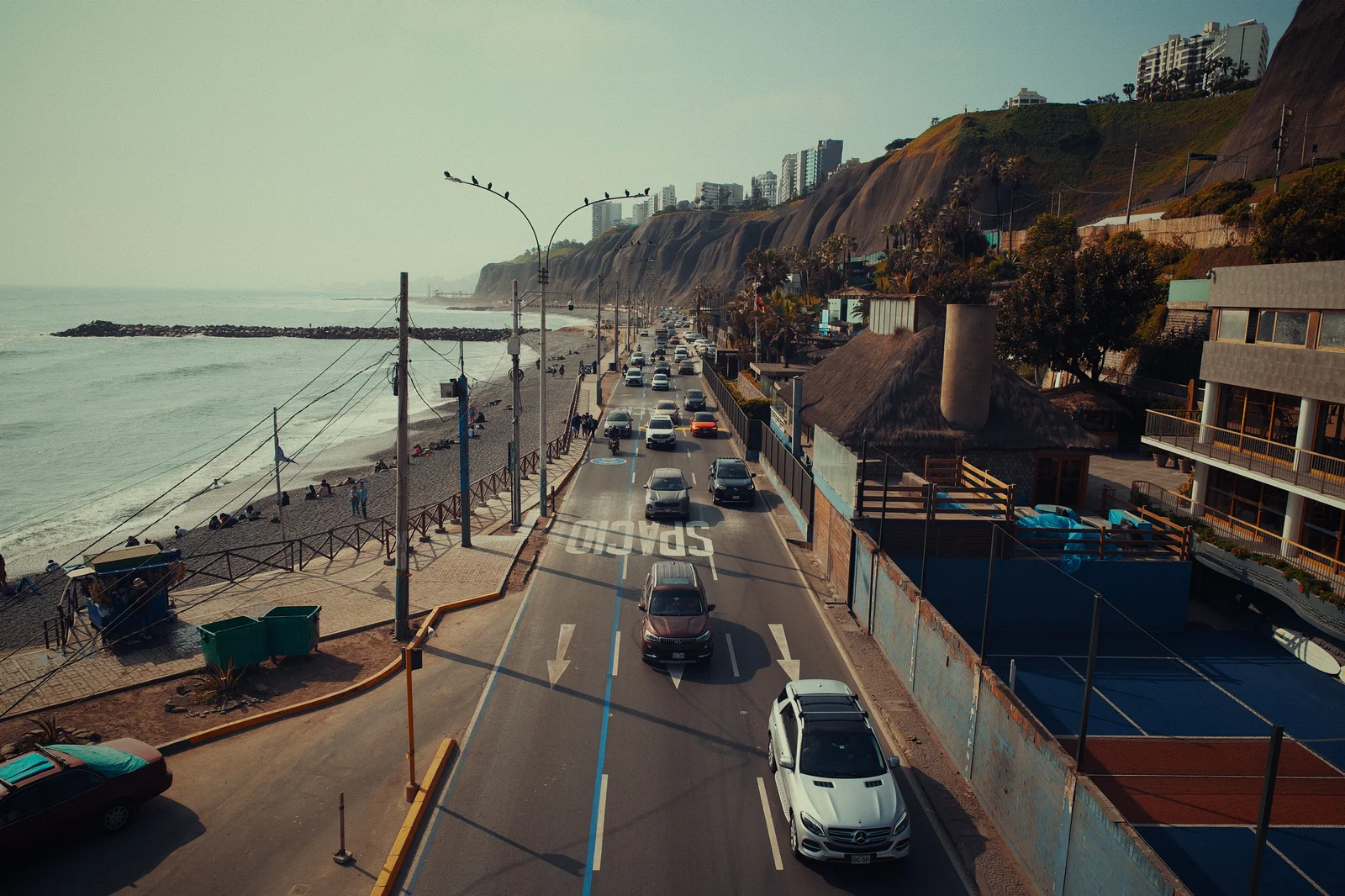 Elevated view of a coastal highway running alongside a beach, city rising on cliffs in the background