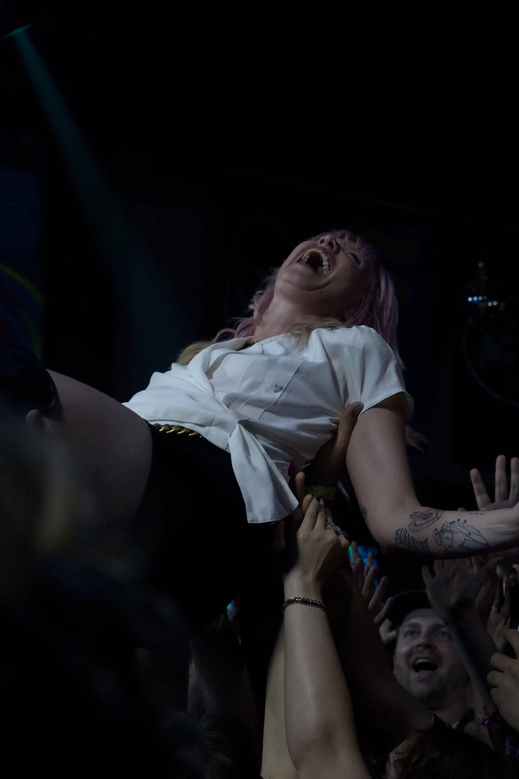 Pink-haired female vocalist throwing her head back while crowd surfing above a sea of hands