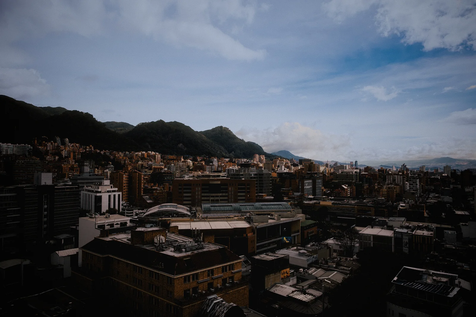 Aerial cityscape of Bogotá, Colombia with dense urban buildings and a green mountain backdrop