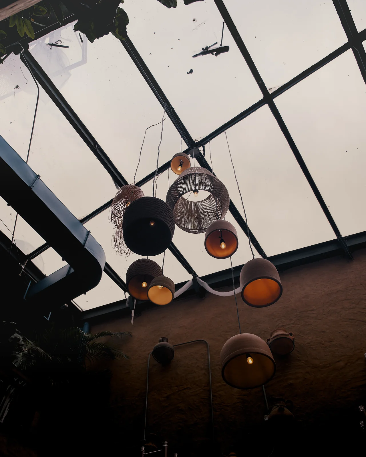 Looking up at eclectic pendant lamps hanging from a glass-paneled skylight ceiling in a restaurant