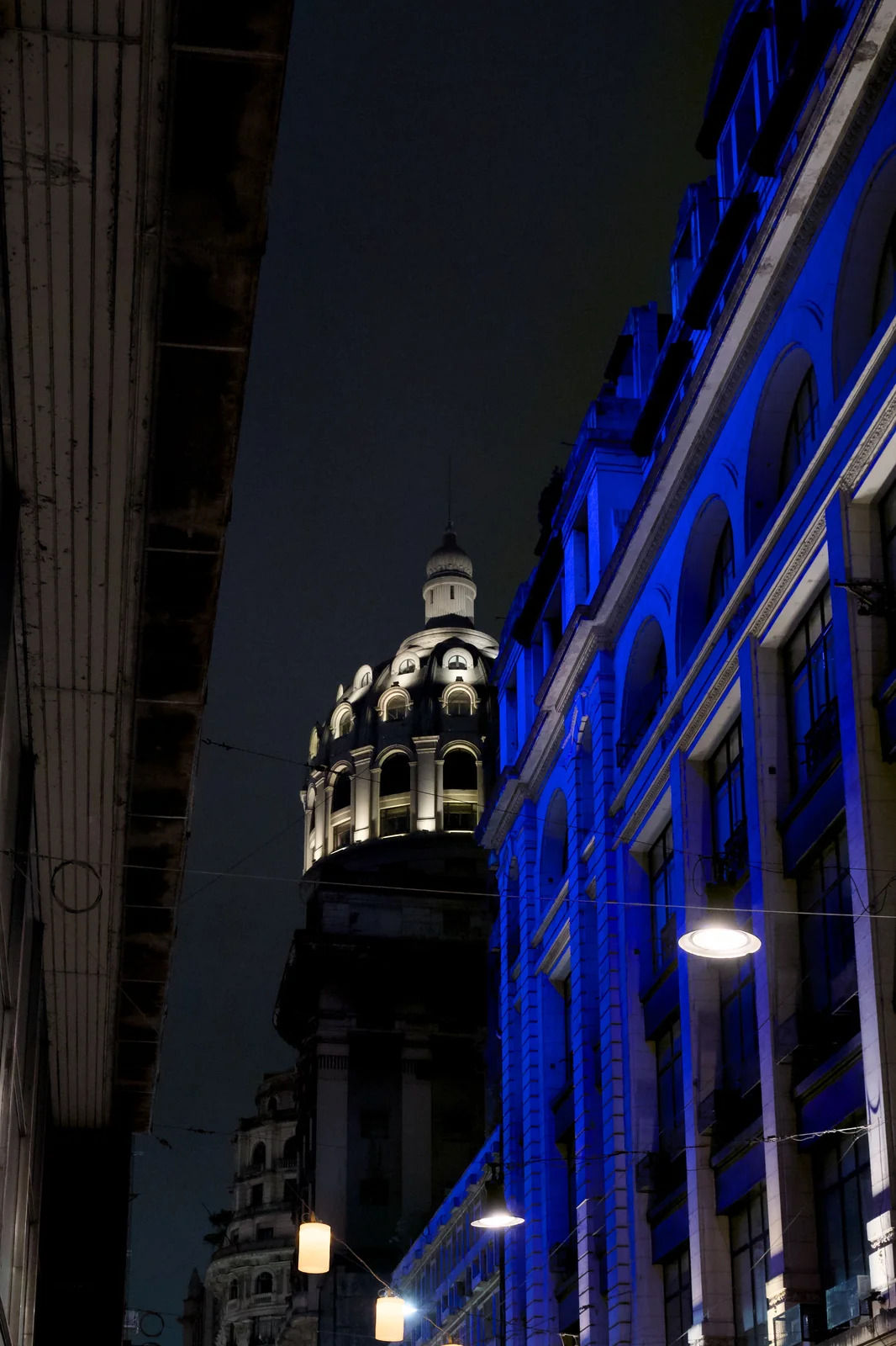 Historic domed building lit with electric blue lights at night along a city street