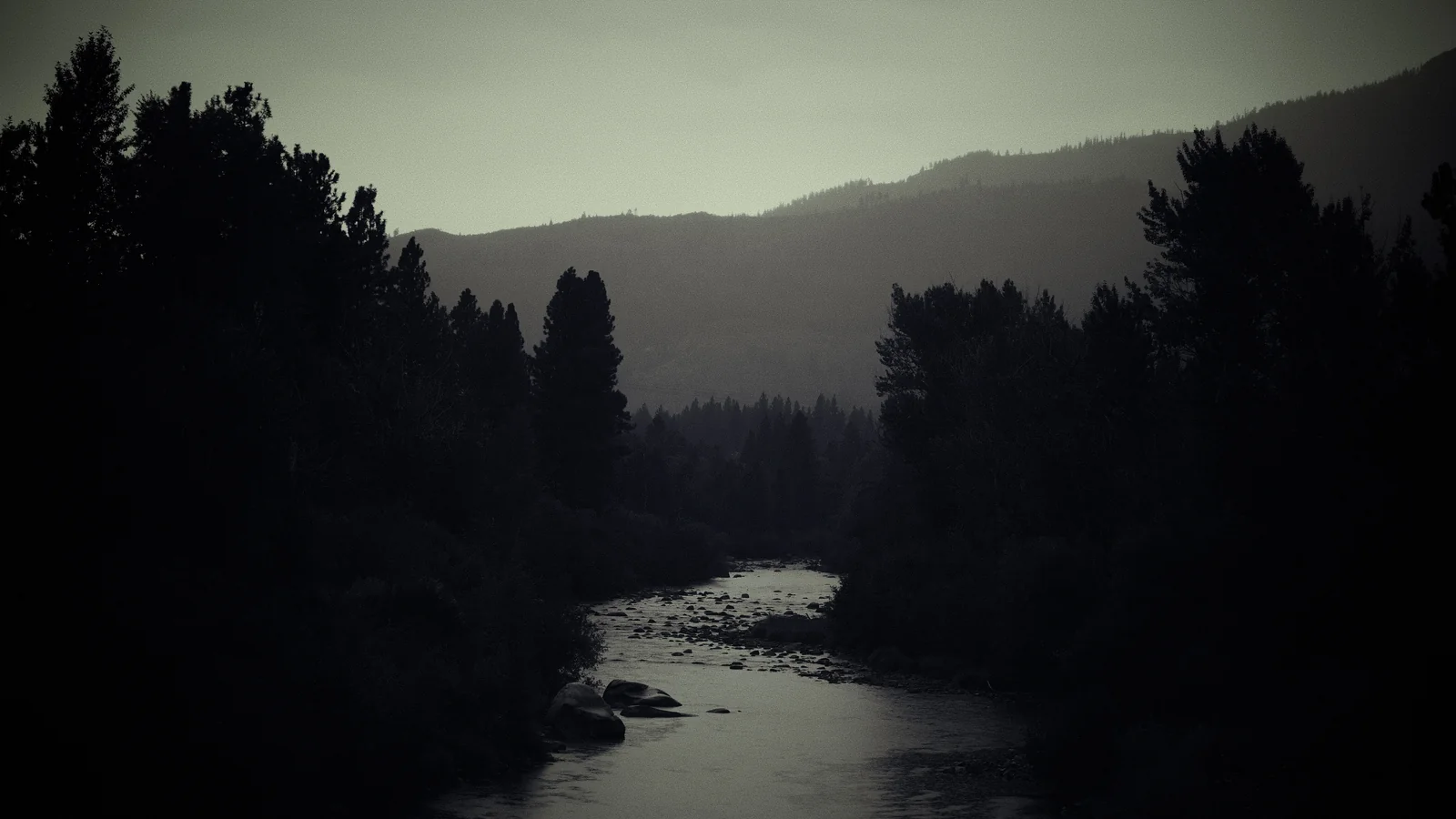Dark moody river winding through a forested mountain valley at dusk