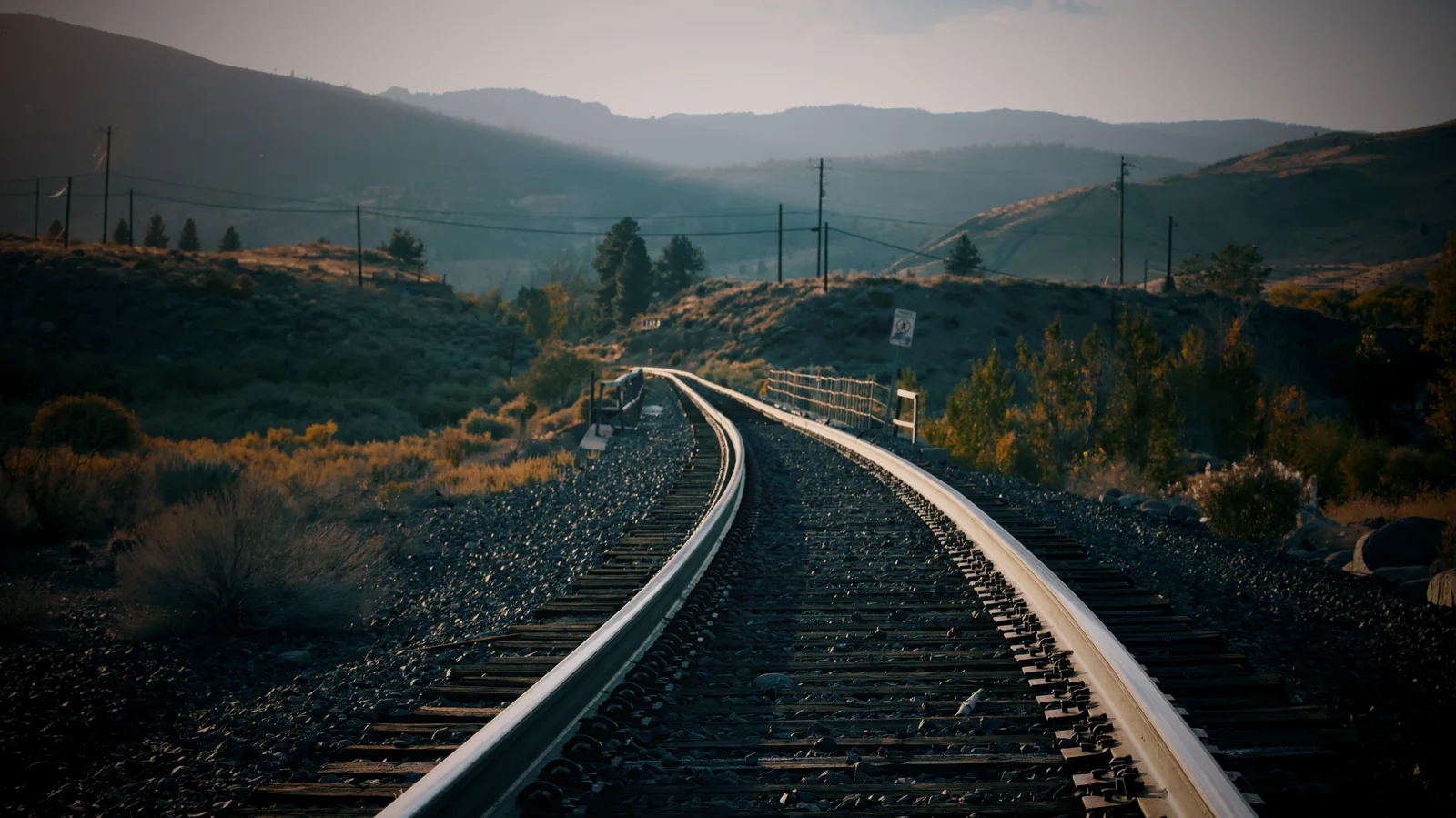 Railroad tracks curving into the distance through a high desert valley at golden hour
