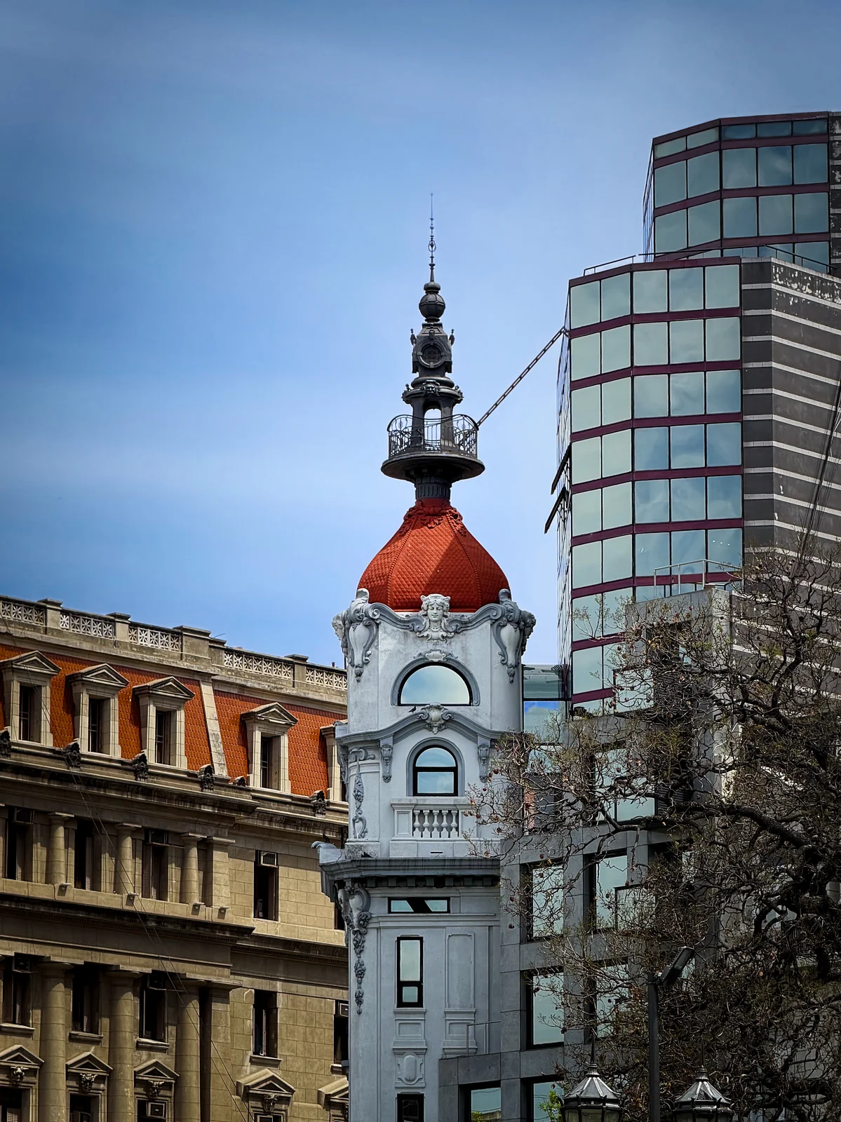 Ornate historic building tower with a red domed roof and decorative iron spire against a blue sky