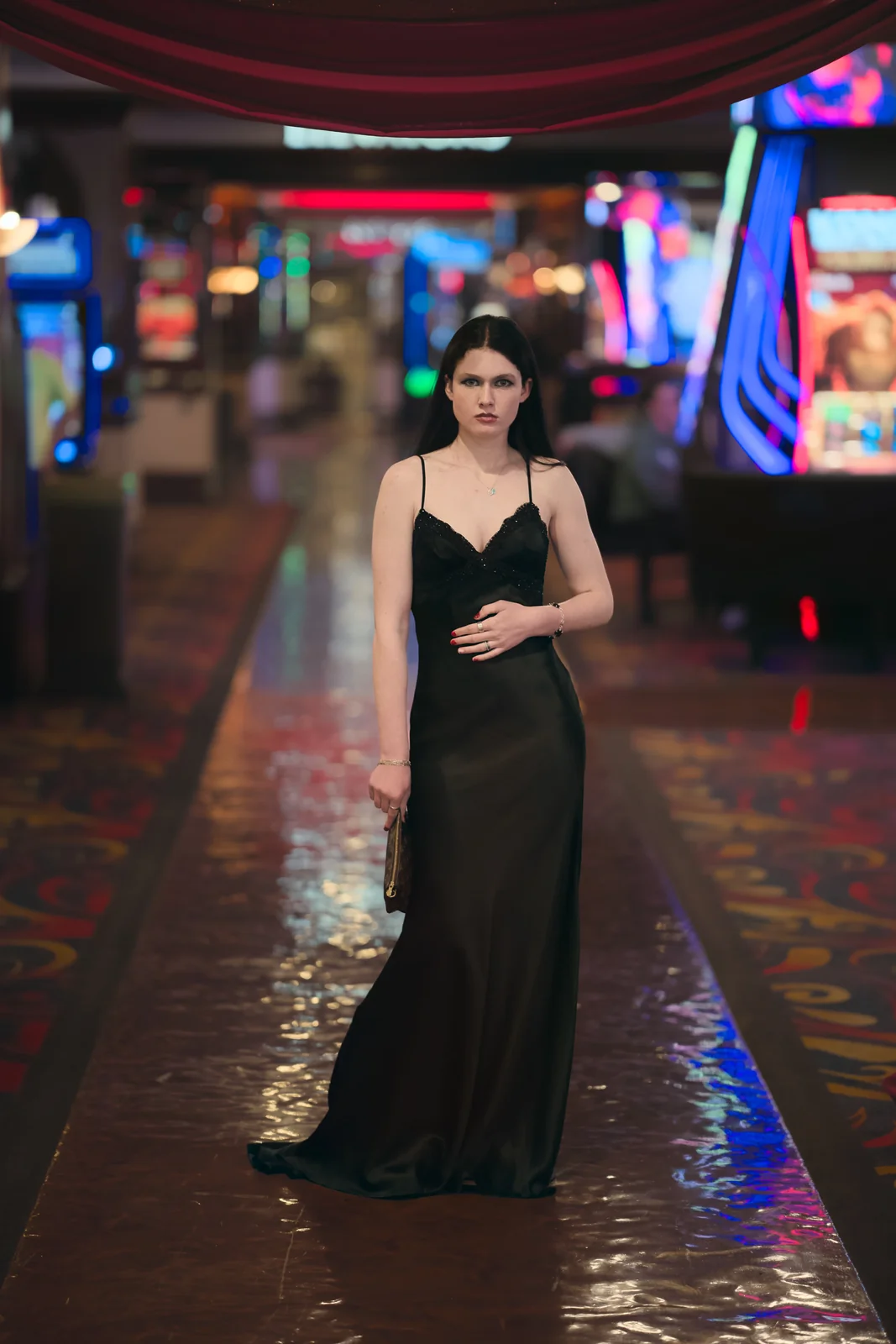 Woman in a black formal gown standing in the aisle of a glittering casino floor