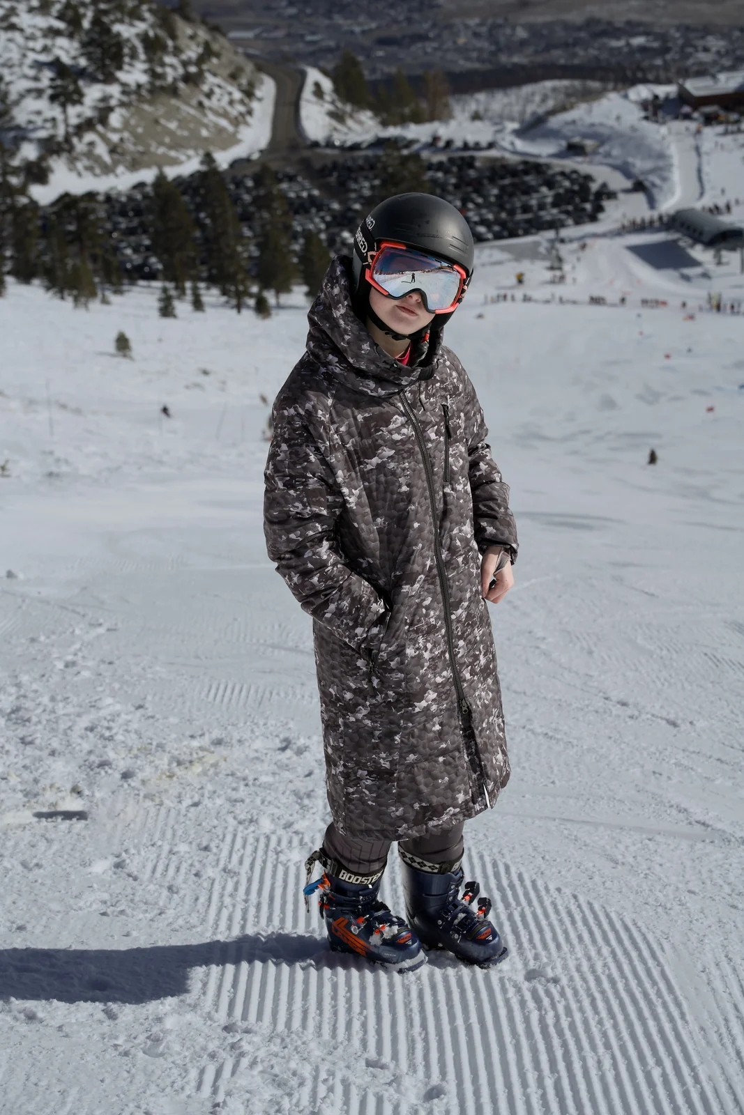 Young child in full ski gear with helmet and goggles standing on a groomed ski slope