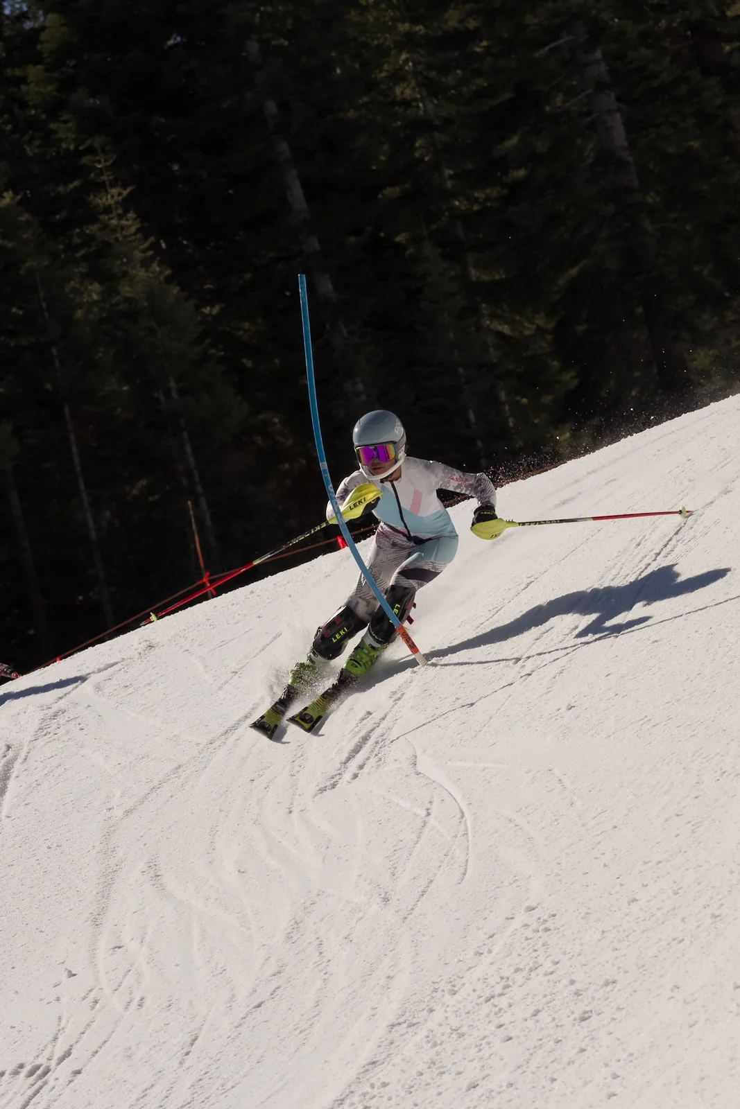 Skier in a white and blue race suit with a pink-visor helmet hitting a blue slalom gate on a sunny slope