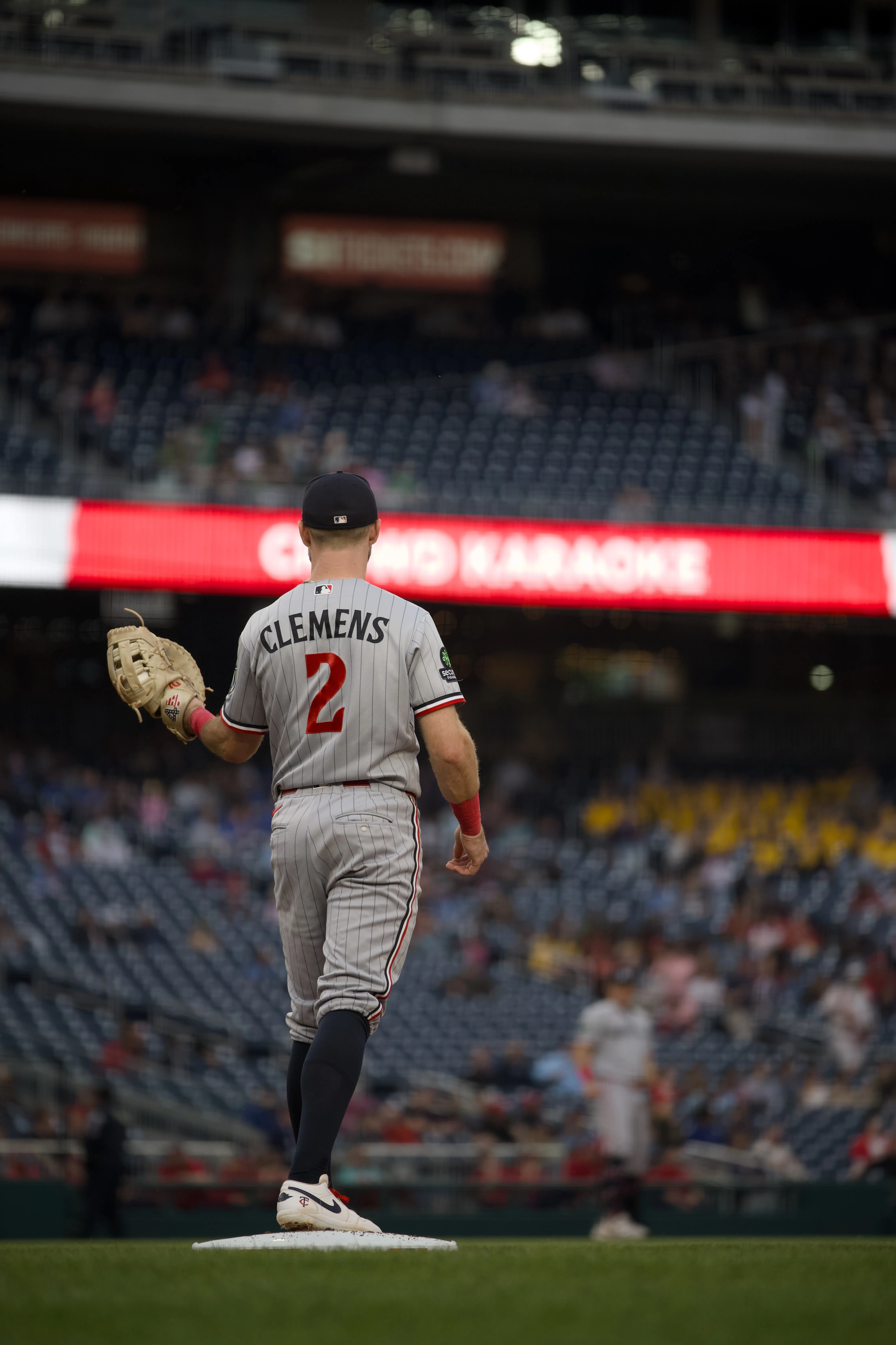Clemens #2 in grey pinstripe road uniform standing at first base from behind, Nationals Park scoreboard glowing in the background