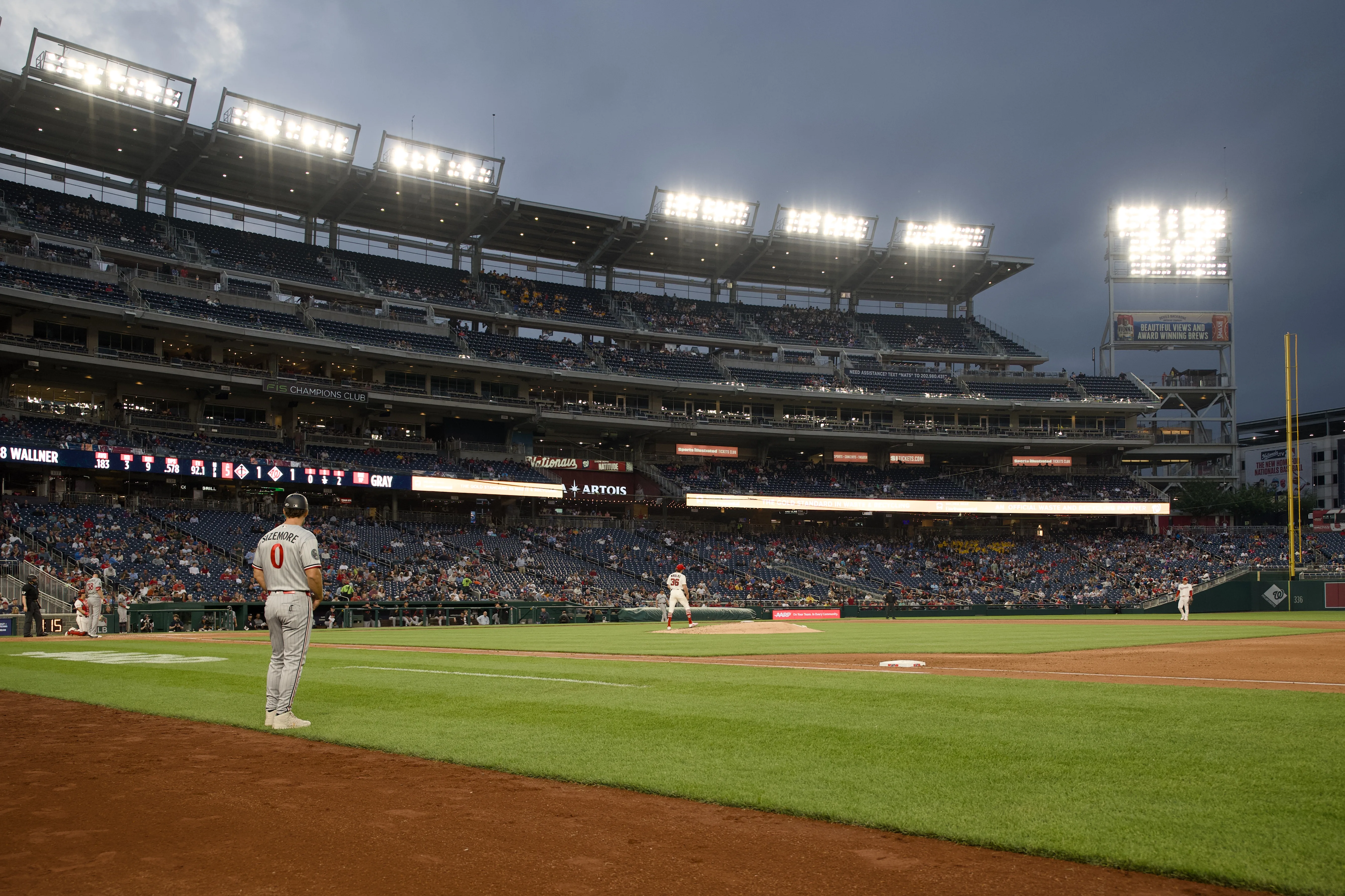 Wide-angle night view of Nationals Park with a player holding position at first base and a batter at the plate under bright stadium lights