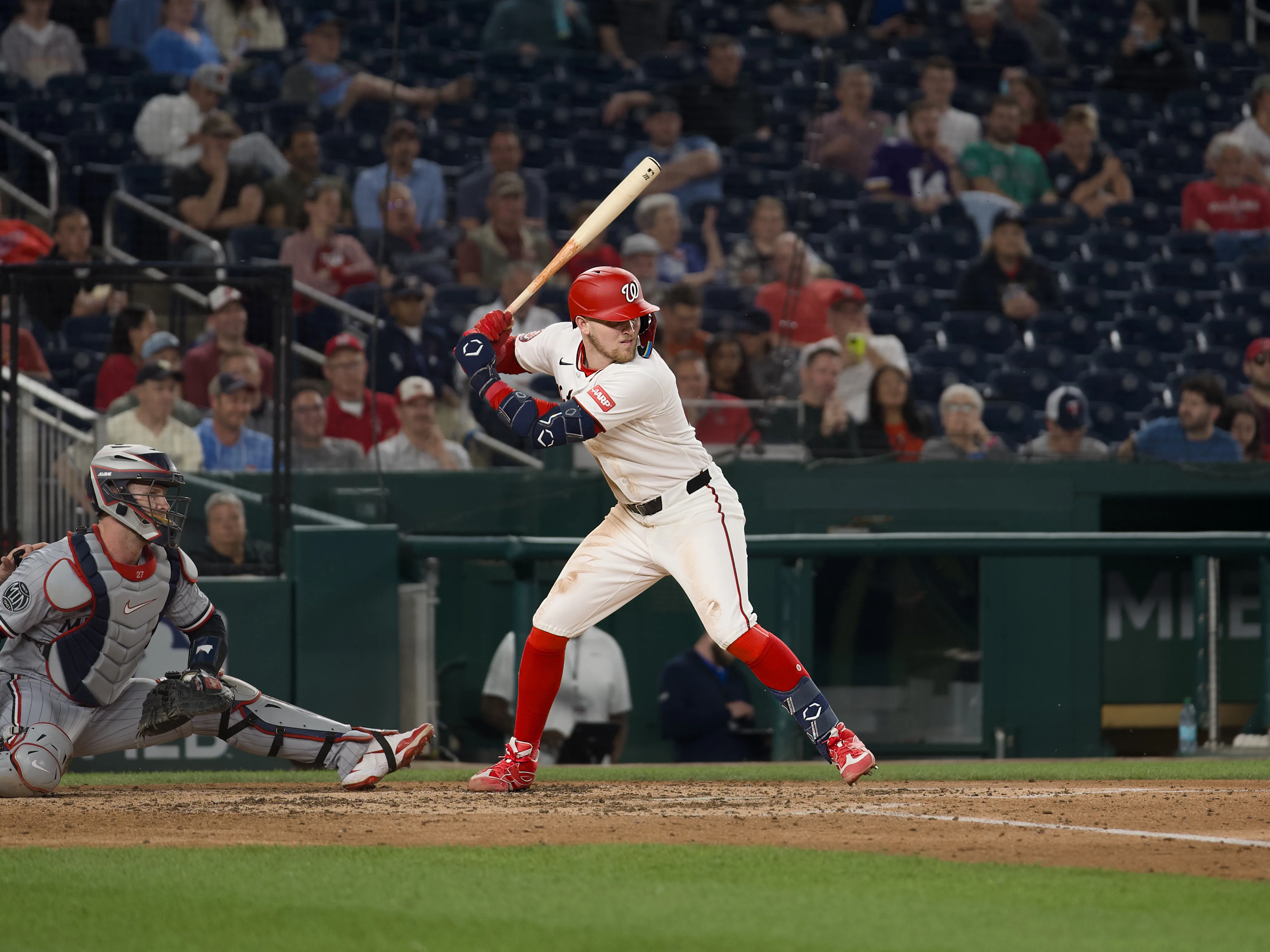 Nationals batter #0 in full batting stance at the plate with catcher crouching behind and a crowd-filled stadium at night
