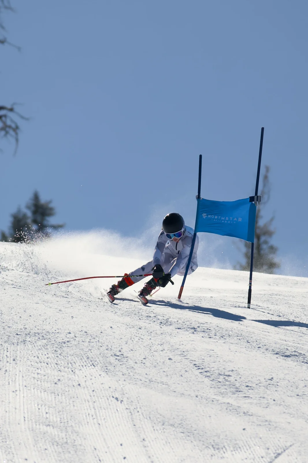 Skier in a white suit charging past a Northstar giant slalom gate under a clear blue sky