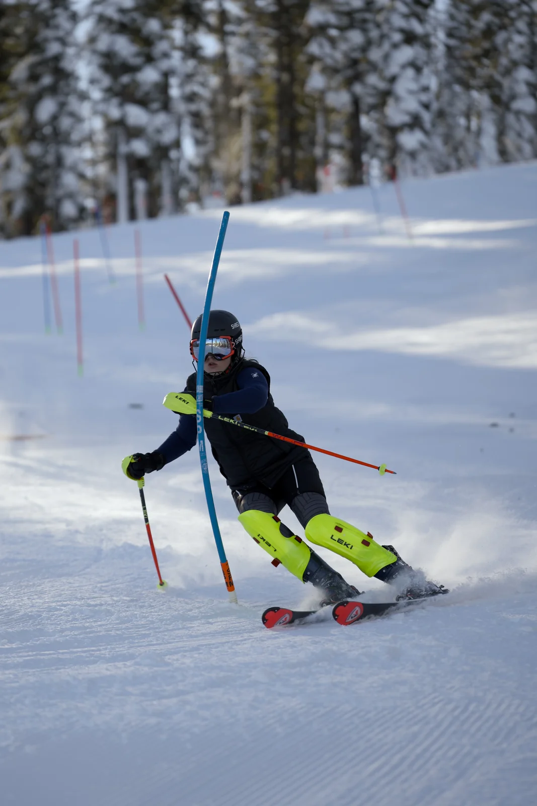 Skier in a dark suit with neon yellow knee guards threading a blue slalom gate